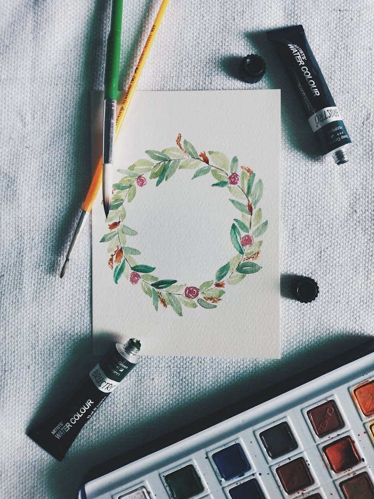 Floral watercolor art with paint tubes and brushes on white cloth.