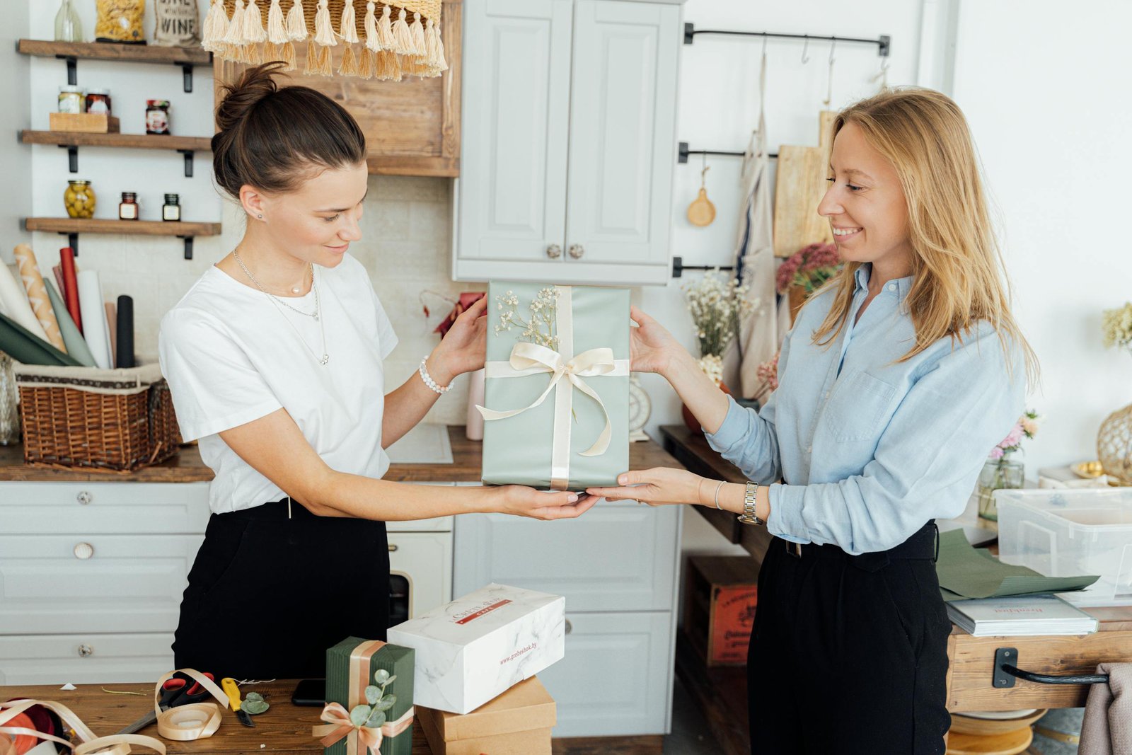 Two women in a home office exchanging a beautifully wrapped gift, symbolizing friendship and celebration.