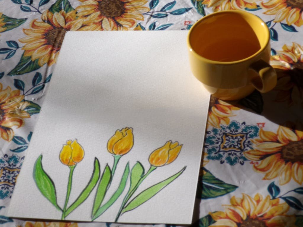 Colorful tulip sketch alongside a yellow mug on a sunflower-patterned tablecloth.