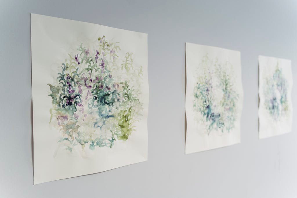 Three watercolor paintings with abstract leaf designs hanging on a light-colored wall.